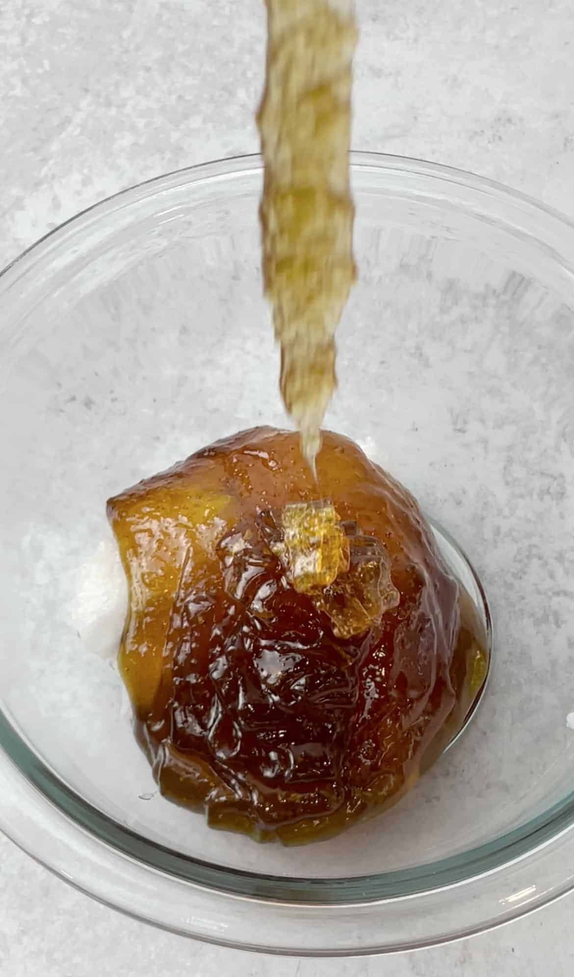 A mixture of honey, eggs, coconut oil, and vanilla extract is being poured in a transparent bowl.