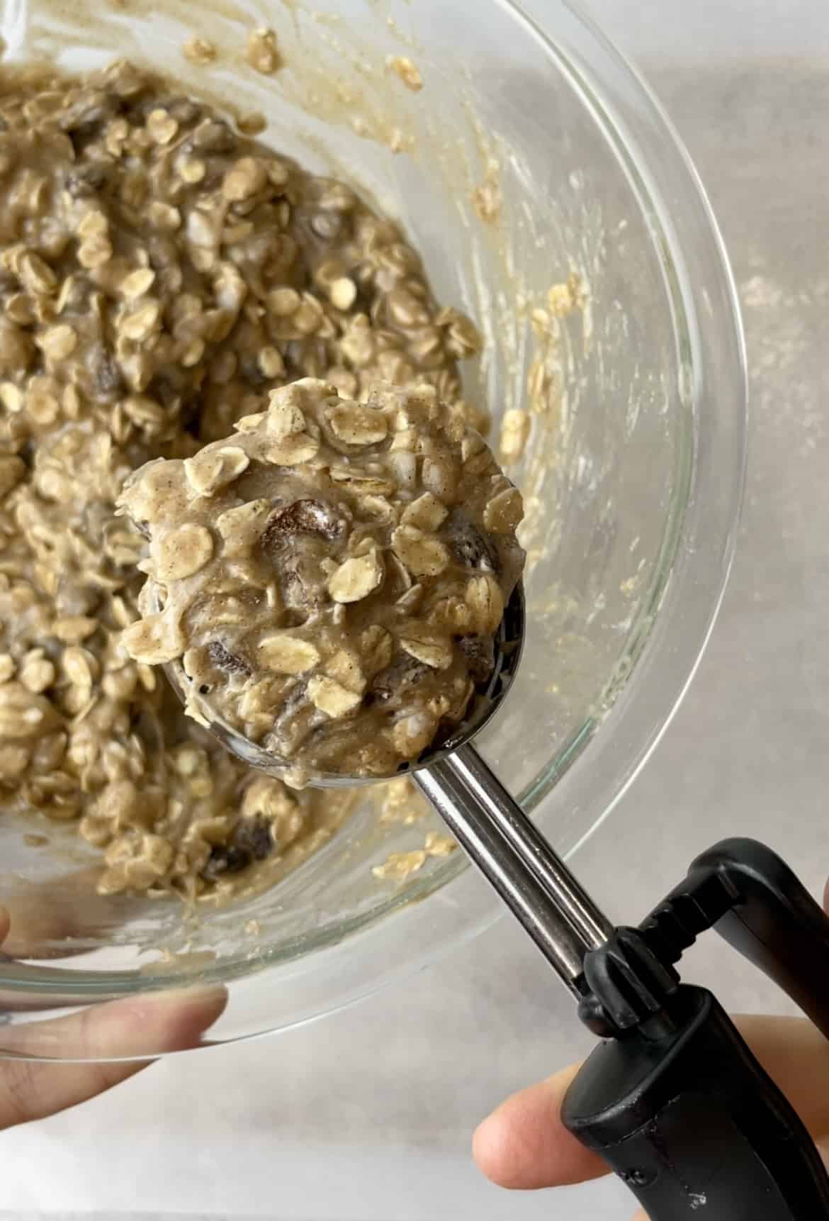 Some oatmeal raisin cookie dough being scooped out of the transparent glass bowl.