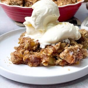 a close shot of apple crisp with oats served on a white plate and topped with whipped cream