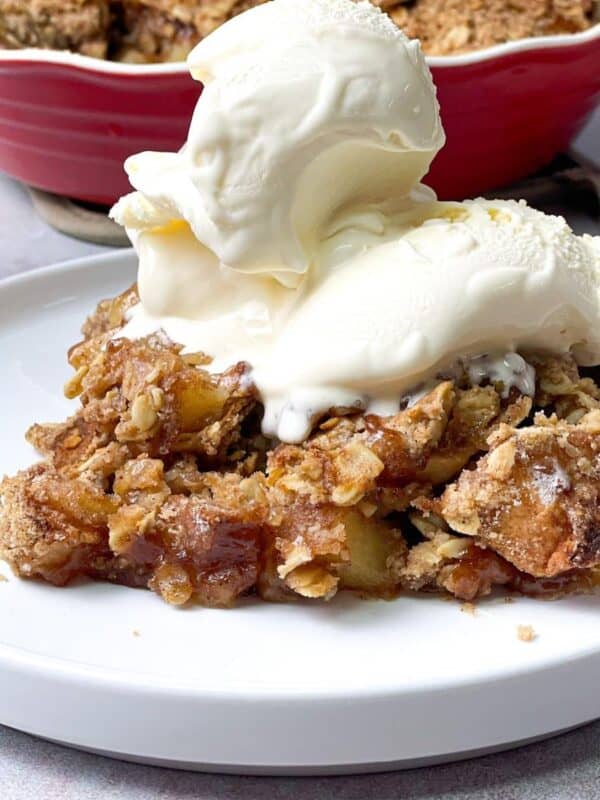 a close shot of apple crisp with oats served on a white plate and topped with whipped cream