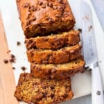 a shot of chocolate chip banana bread sliced ​​in half, placed on a serving plate next to a sharp knife, and the slices of the other half