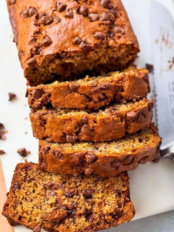 a shot of chocolate chip banana bread sliced โโin half, placed on a serving plate next to a sharp knife, and the slices of the other half