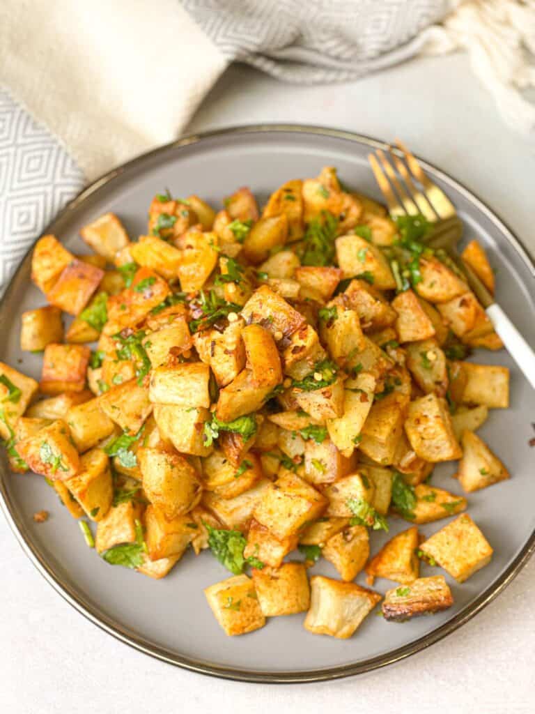 In a metal plate, roasted potato cubes are placed. They are drizzled with with fresh coriander, garlic and chili powder.