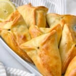 Golden-brown Lebanese spinach pies arranged on a white dish, showcasing their triangular shape and perfectly baked crust.