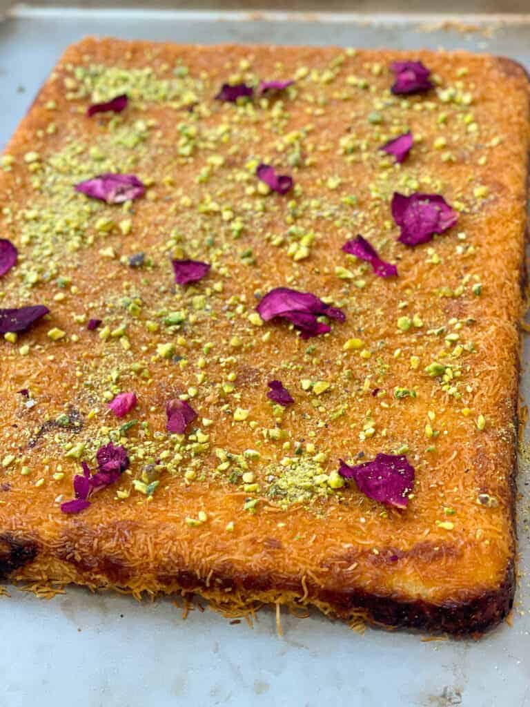 Knefeh: A traditional Middle Eastern dessert made of shredded phyllo dough layered with sweet cheese, baked to golden perfection, and drizzled with syrup, garnished with pistachios.