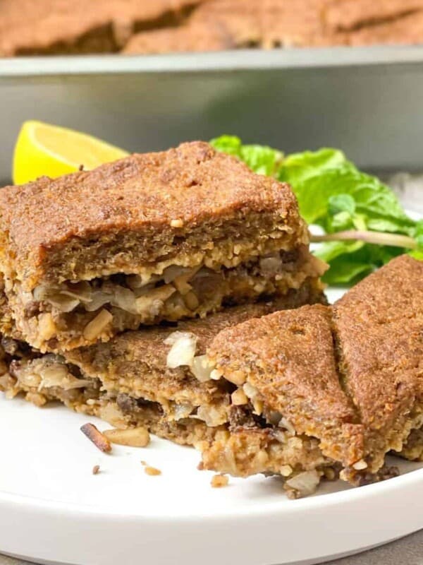 Two pieces of baked kibbeh served in a white plate with a lemon wedge and fresh mint