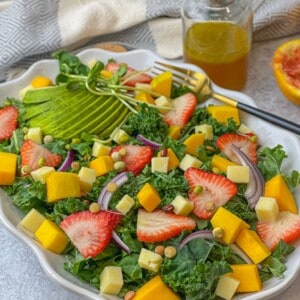 a salad tray made up with kale, strawberry, mango, red onion, avocado, cheddar cheese, and lentil sprouts, and glazed with citrus vinaigrette with oranges