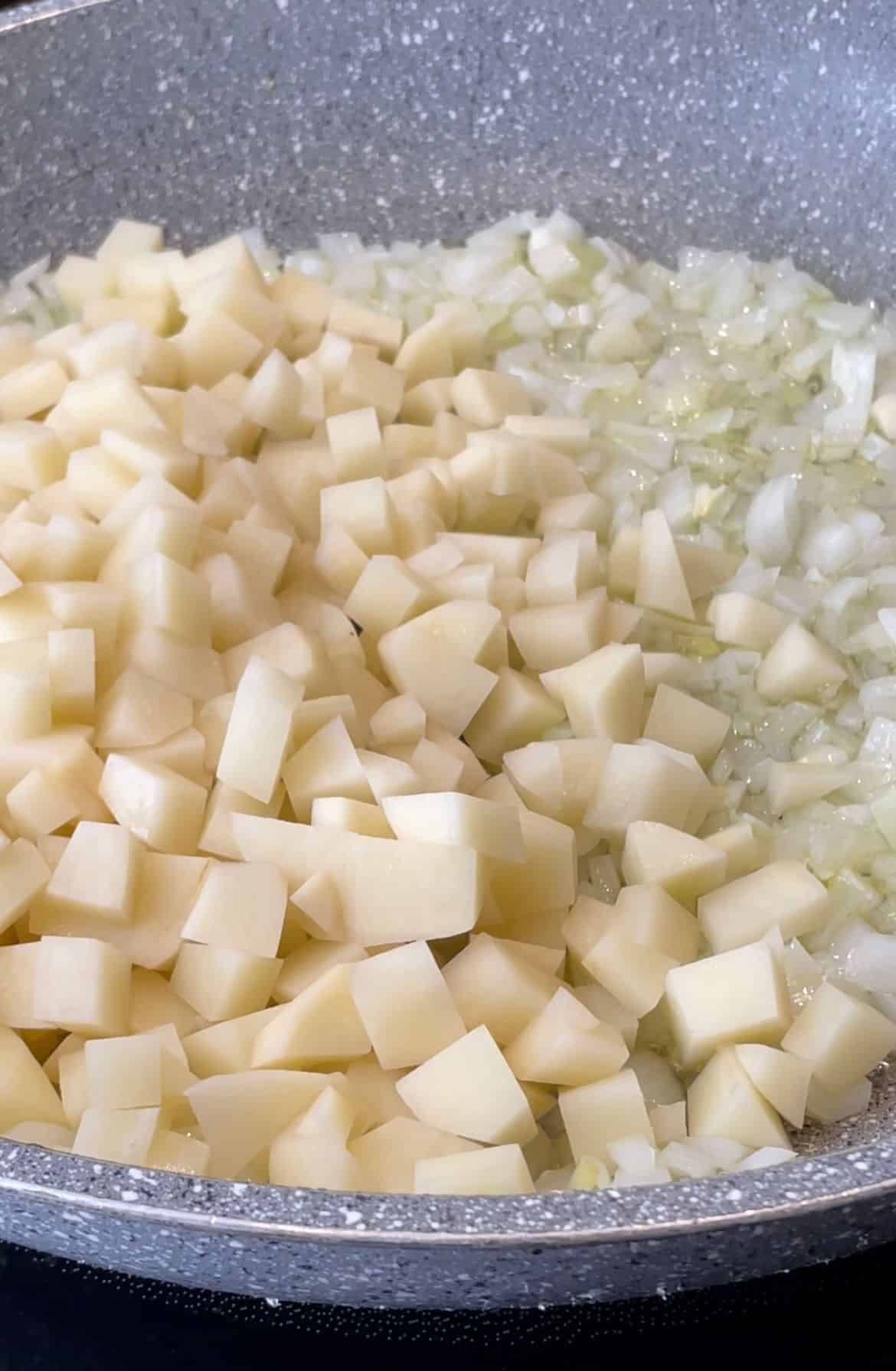 cubed potatoes that are added to a skillet of sautéed onions