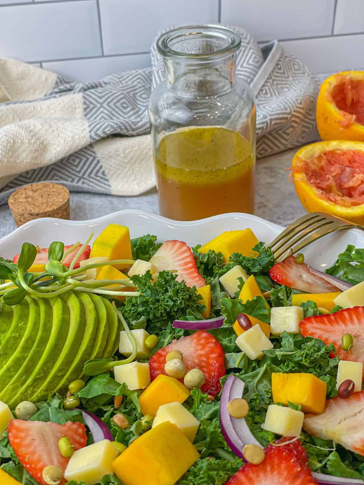 a tray of colorful salad made up of fresh veggies and fruits and placed next to a jar of citrus vinaigrette dressing