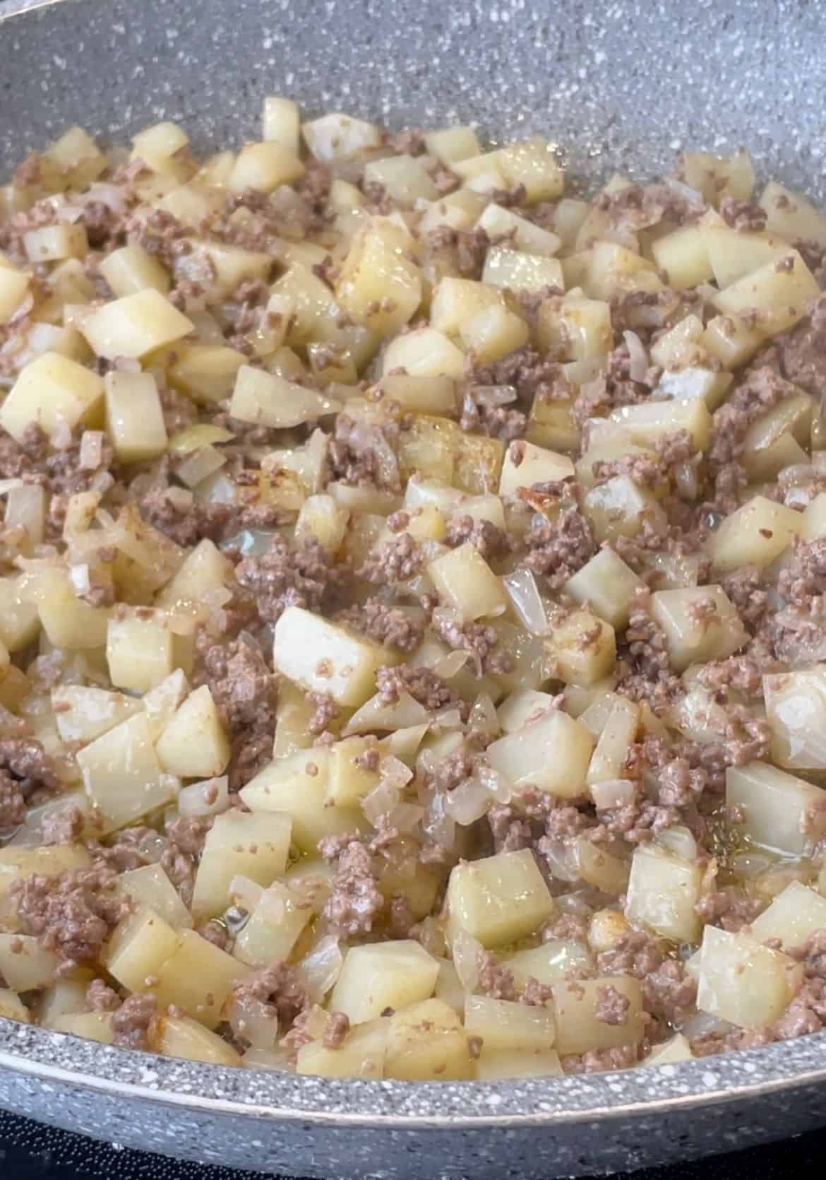 a skillet that contains sauteed onions, potatoes, and ground beef