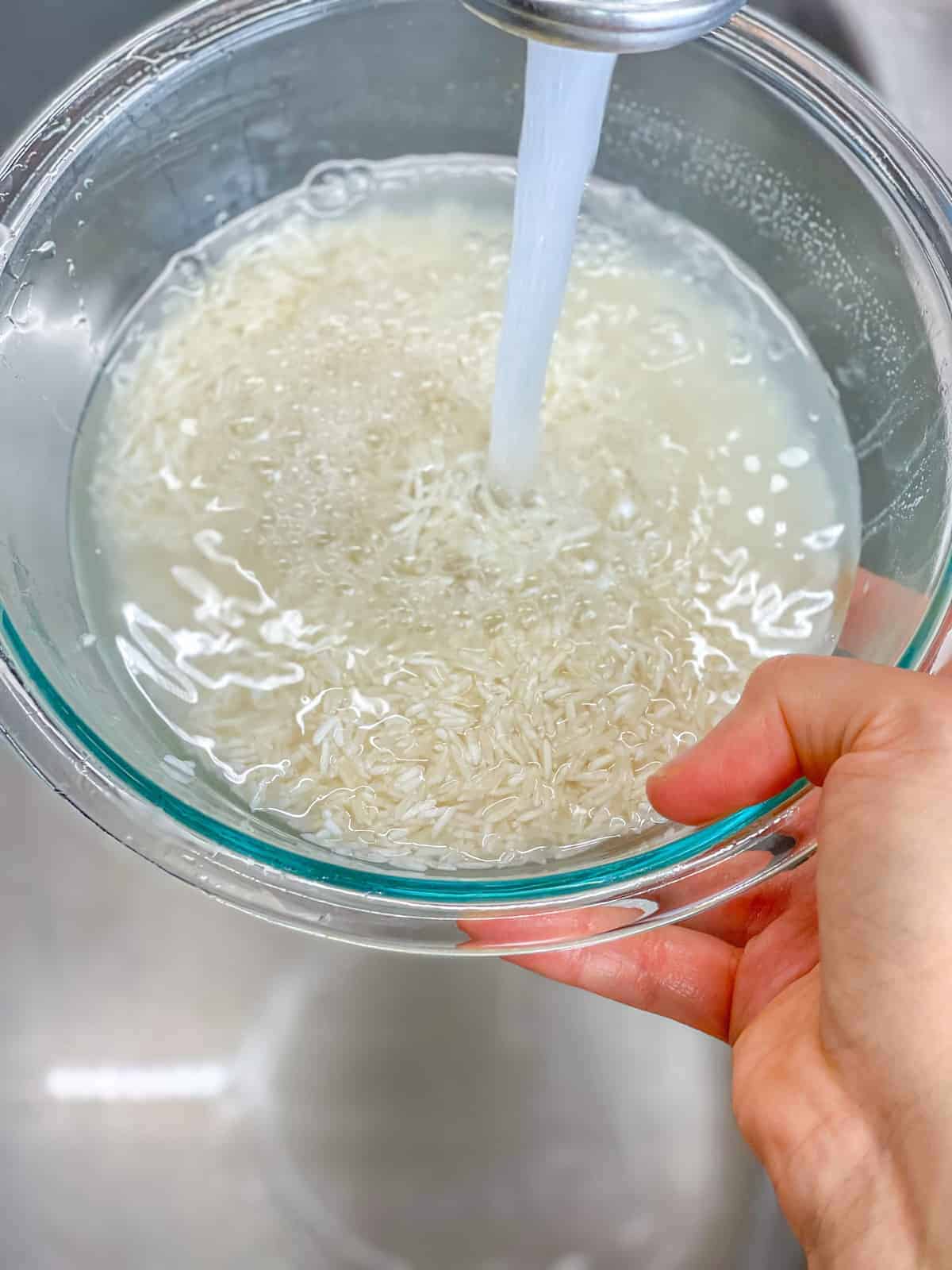 a women washing rice grains in a medium glass bowl