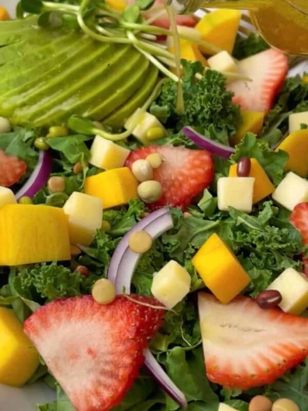 a colorful salad made up of kale, strawberry, mango, red onion, avocado, cheddar cheese, and lentil sprouts