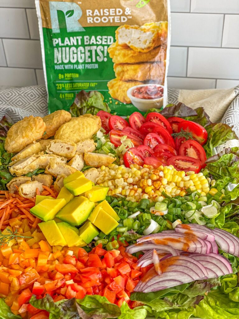 a plant-based salad dish made up of lettuce, corn, tomatoes, red and green onions, avocado, shredded carrots, colored peppers, and plant-based nugget