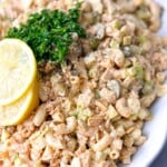 A bowl of tuna egg salad, featuring a creamy mixture of flaked tuna, chopped hard-boiled eggs, mayonnaise, and finely diced vegetables such as celery and onion, garnished with a sprinkle of paprika. The salad is served on a white plate with a fork on the side.