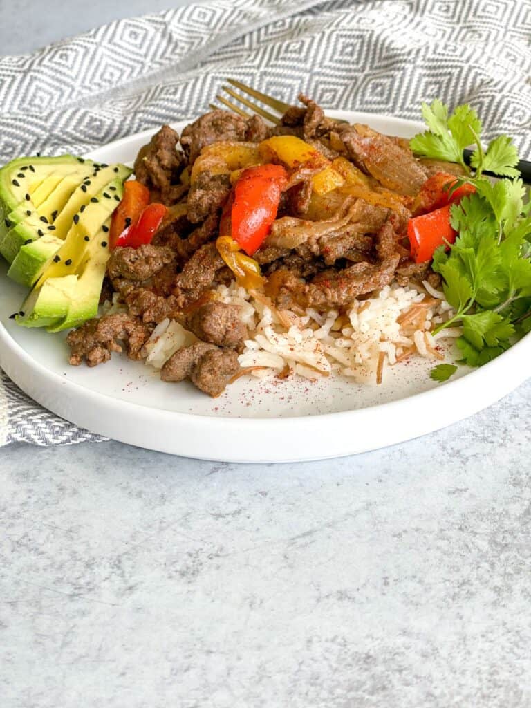A hearty beef steak fajita bowl with peppers and onions on a bed of white vermicelli rice and a side of avocado