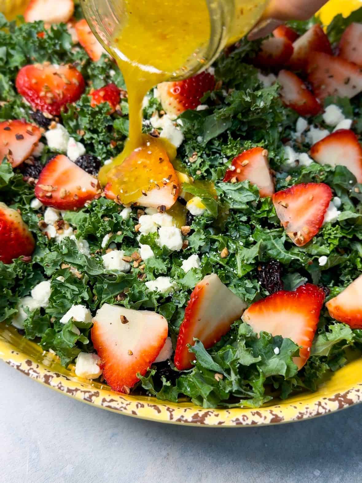 Kale Salad Dressing drizzling Dijon dressing over a colorful Kale Salad with strawberries, cranberries, pecans, and feta cheese.