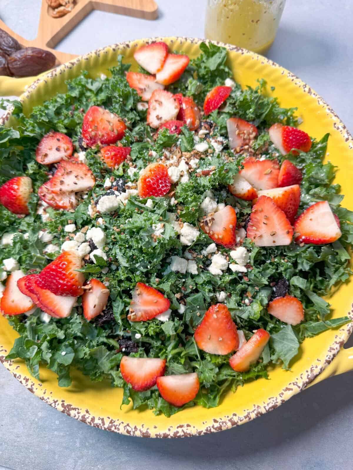 Close-up of Kale Dijon Salad in a bowl, showcasing the mix of leafy greens, strawberries, and crumbled feta.