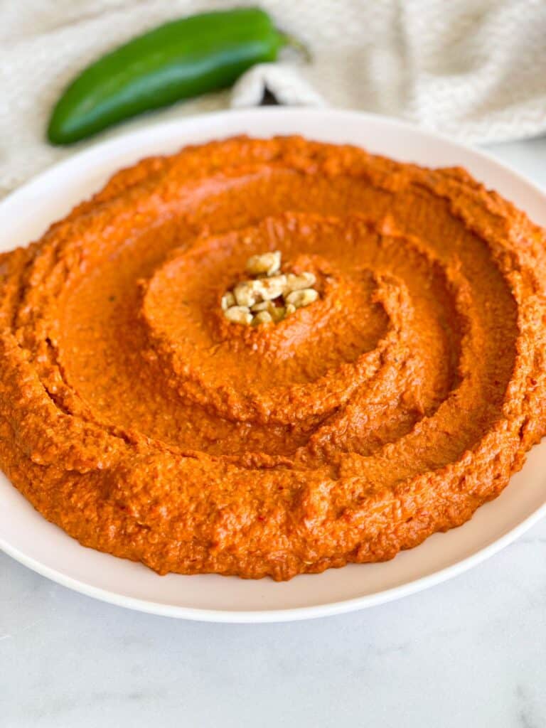 A dish of homemade Muhammara dip made with roasted red pepper and walnuts. A dish of creamy texture, smoky flavor, and a vibrant red color.