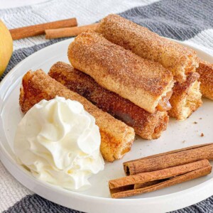 Baked apple pie rolls are filled with gooey apple pie filling, coasted with sugar and cinnamon, and served with fresh whipped cream.