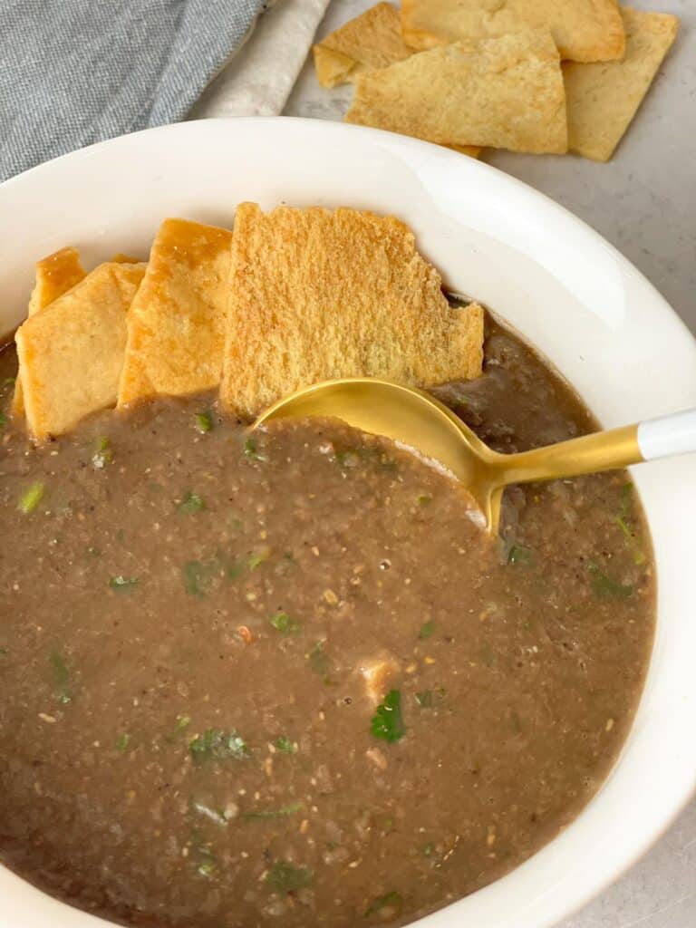 A delicious warm bowl of brown lentil soup, blended together with rice and has savory ground beef and green parsley and a side of salted crackers
