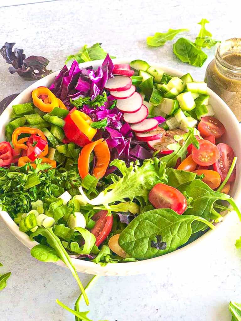 Roma tomatoes, romaine lettuce, cucumbers, onions, and radishes are all mixed up in a bowl with savory dressing made in a tabletop blender.