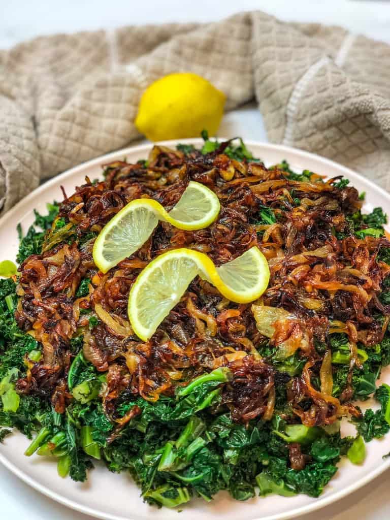 The Kale Salad with Caramelized Onions  is a delicious salad that is comprised of golden crunchy onions on moist and fluffy kale. The lemon slices are placed over the golden onions as a finishing touch.