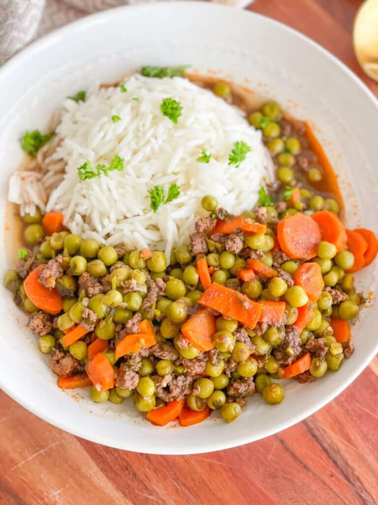 This Lebanese Peas and Carrots Stew also known as Bazella w Riz is a comfort stew that is easy to prepare. It is made with ground beef, carrots, peas and garlic, all simmered in a rich tomato sauce. It's served on a bed of white rice.
