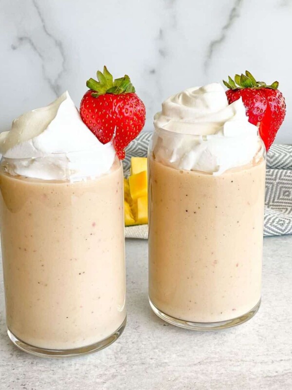 Two glasses filled with fresh strawberry banana smoothie topped with whipped cream and decorated with strawberries.
