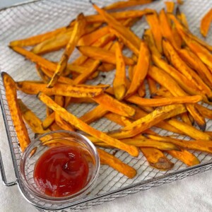 A tray of sweet potato fries with some ketchup on the side.