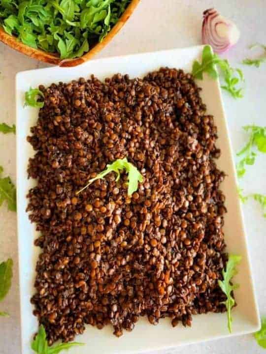 A rectangular plate contains a traditional Lebanese recipe called Mjadara Hamra. It is made with red lentils and bulgur and served with fresh veggies.