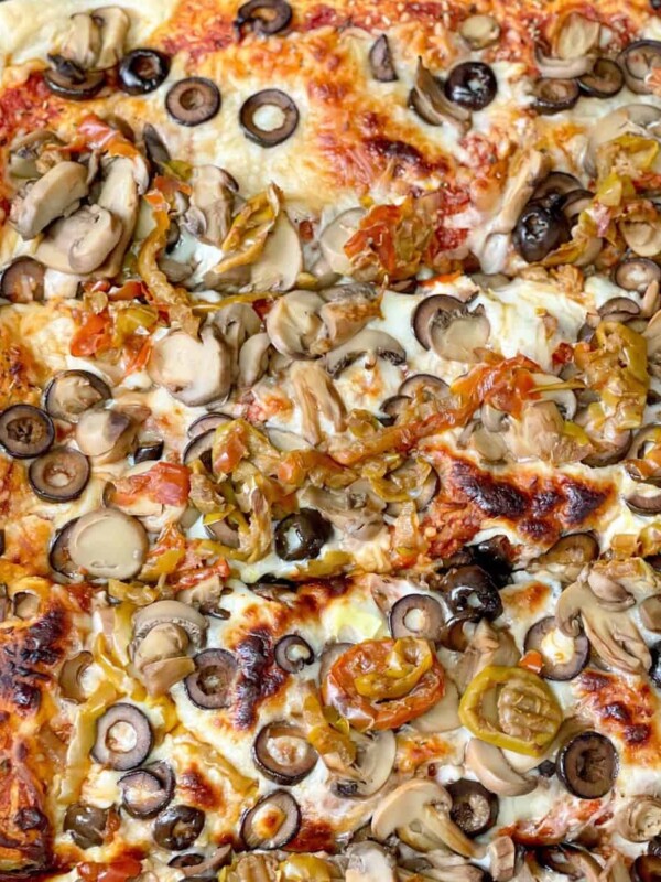 A baked pizza dough toped with cheese, veggies, mushrooms and black olives.
