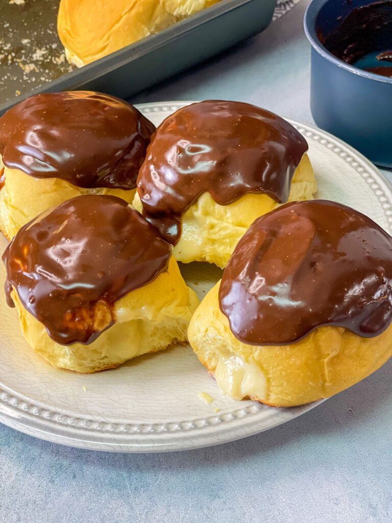 Soft and tender brioche buns filled with a creamy custard filling and topped with chocolate ganache.