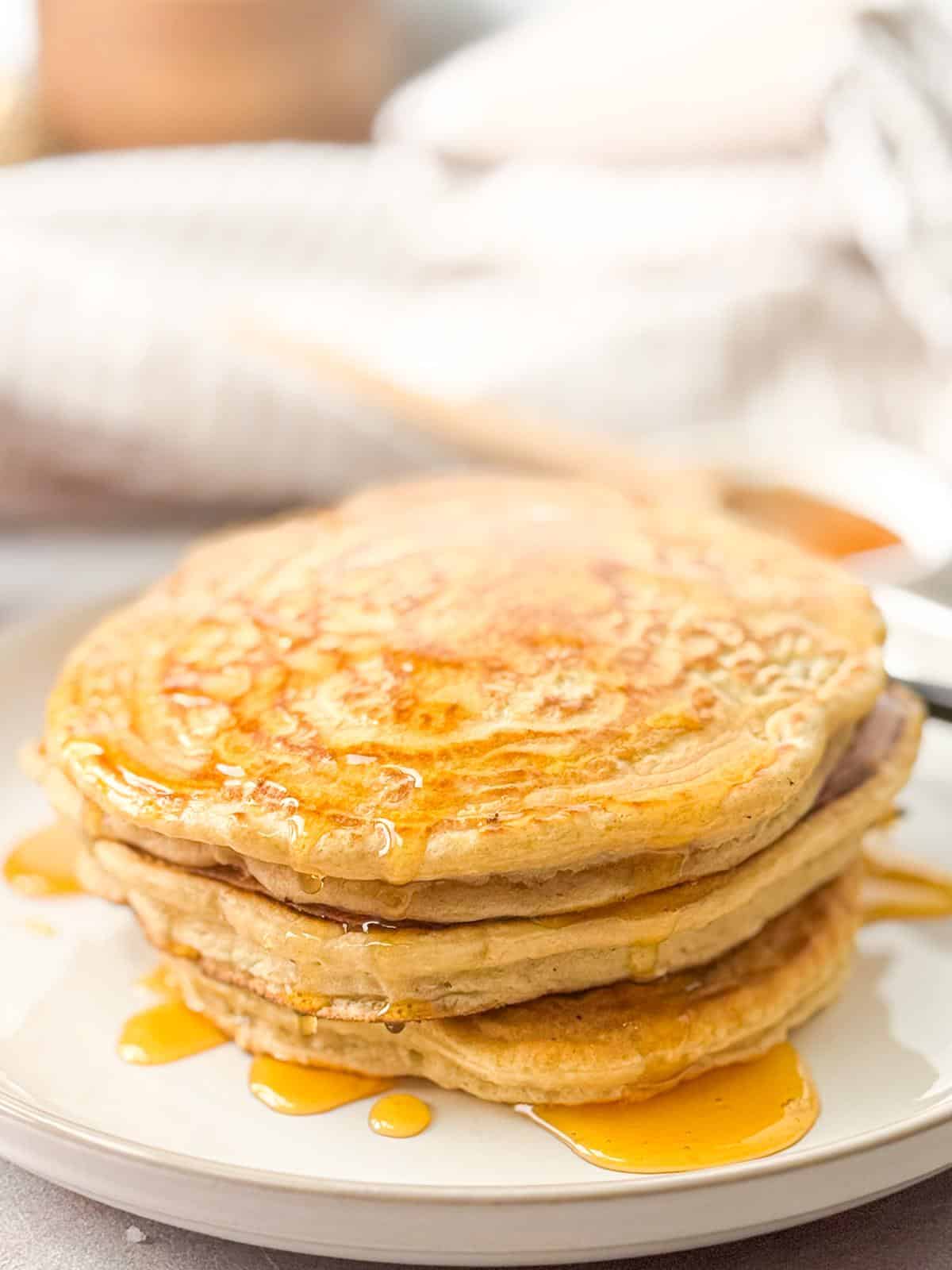 Single Serve Fluffy Pancakes A stack of golden, fluffy pancakes, served on a white plate, glistening with syrup that drips down the sides.