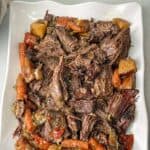 a large plate of easy tender slow cooker roast with tomato, carrots, onions, and potatoes