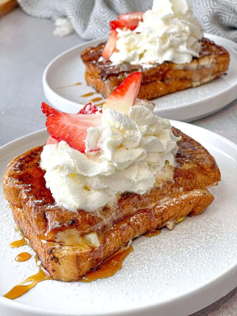 This Brioche Strawberry Cheesecake French Toast presents golden toasty slices of well-seasoned bread stuffed with cream cheese, sugar, and strawberries, and topped with a drizzle of honey, syrup, whipped cream, and fresh strawberries! 