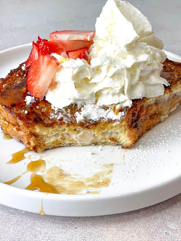 This Brioche Strawberry Cheesecake French Toast presents golden toasty slices of well-seasoned bread stuffed with cream cheese, sugar, and strawberries, and topped with a drizzle of honey, syrup, whipped cream, and fresh strawberries! 