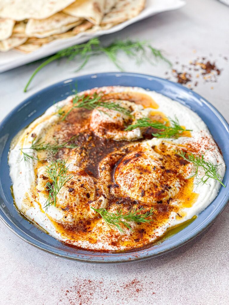 Turkish eggs are set on a creamy layer of yogurt and topped with spiced butter. It is garnished with dill and paprika. Looks perfect!
