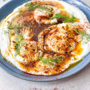 Turkish eggs are set on a creamy layer of yogurt and topped with spiced butter. It is garnished with dill and paprika.
