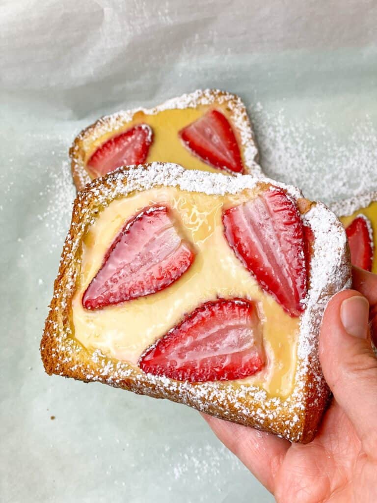A hot slice of custard brioche toast garnished with strawberries ready to be devoured.