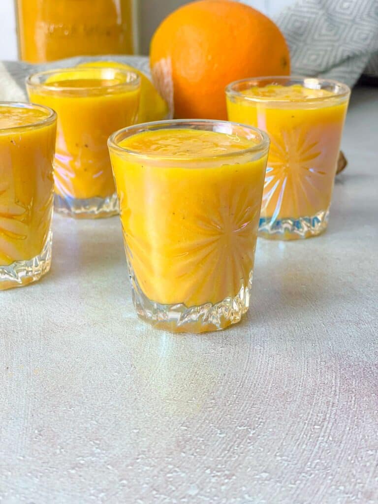 Four small cups of ginger turmeric immunity shots ready to be served for the whole family.
