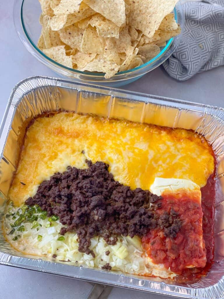 This Taco Queso Dip recipe presents a mix of well seasoned ground beef, spices, and layers upon layers of cheese.
