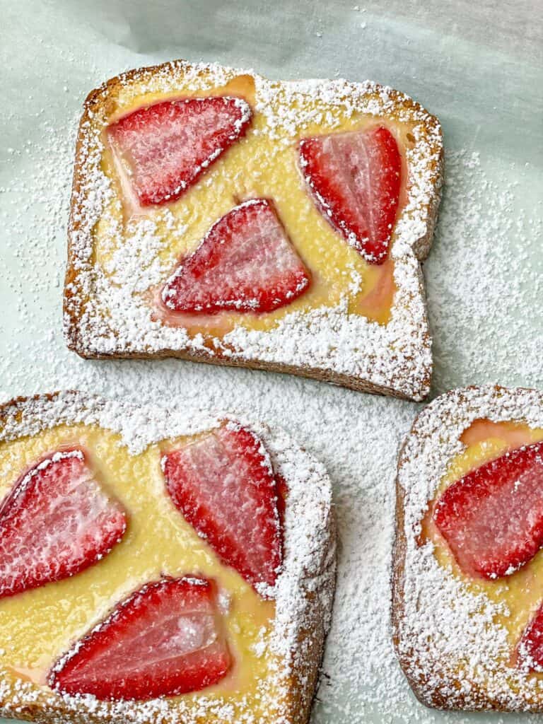 Brioche toast topped with custard and strawberries and sprinkled with confectioners sugar. The perfect breakfast for the whole family.