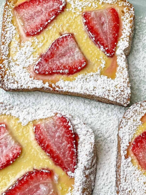 Brioche toast topped with custard and strawberries and sprinkled with confectioners sugar.