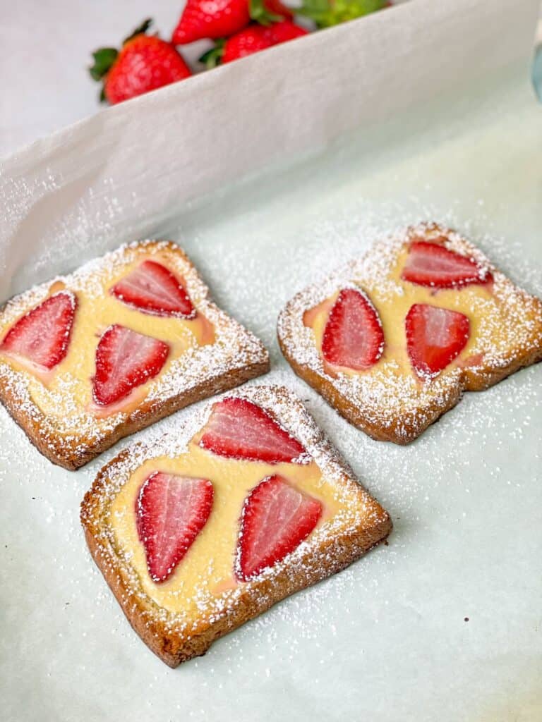 Slices of brioche toast topped with creamy custard and juicy strawberries, A sprinkle of confectioners sugar is added on top to give it a sweet kick.