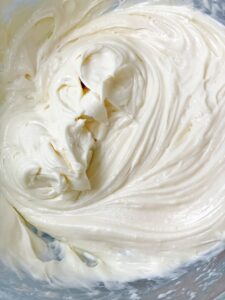 Indulgent cream cheese frosting gracefully piled in a bowl, its creamy texture inviting a delightful culinary experience. The soft, billowy swirls showcase the rich and velvety consistency, promising a heavenly taste that complements any dessert creation.