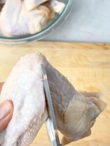 A hand cutting a raw chicken wing with meat scissors.