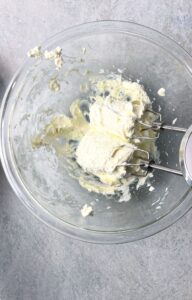 cream cheese frosting ingredients mixed with a hand mixer in a glass bowl