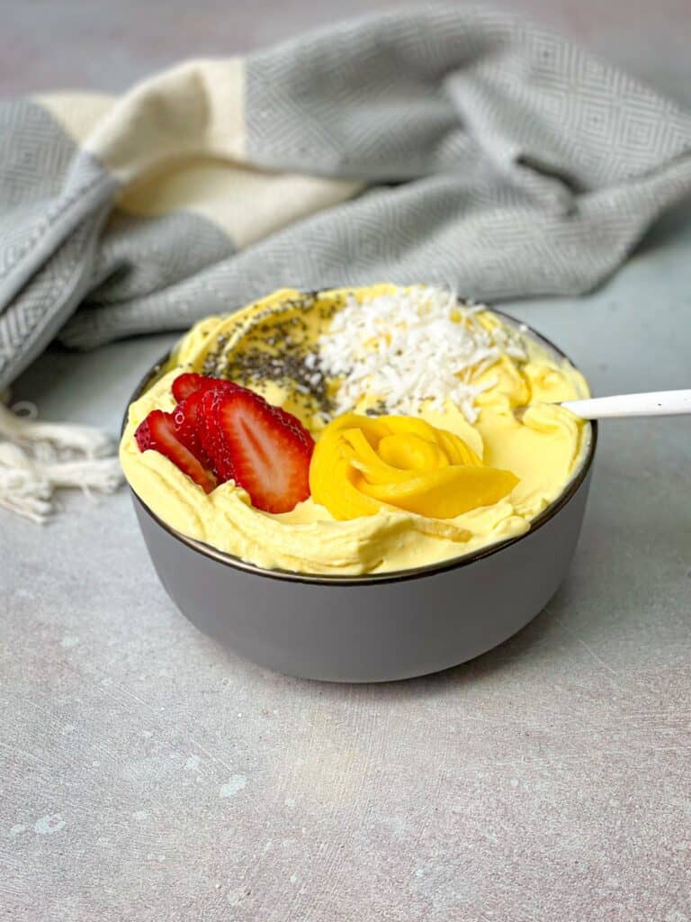 A delicious bowl of mango soft serve is decorated with fruits and seeds.