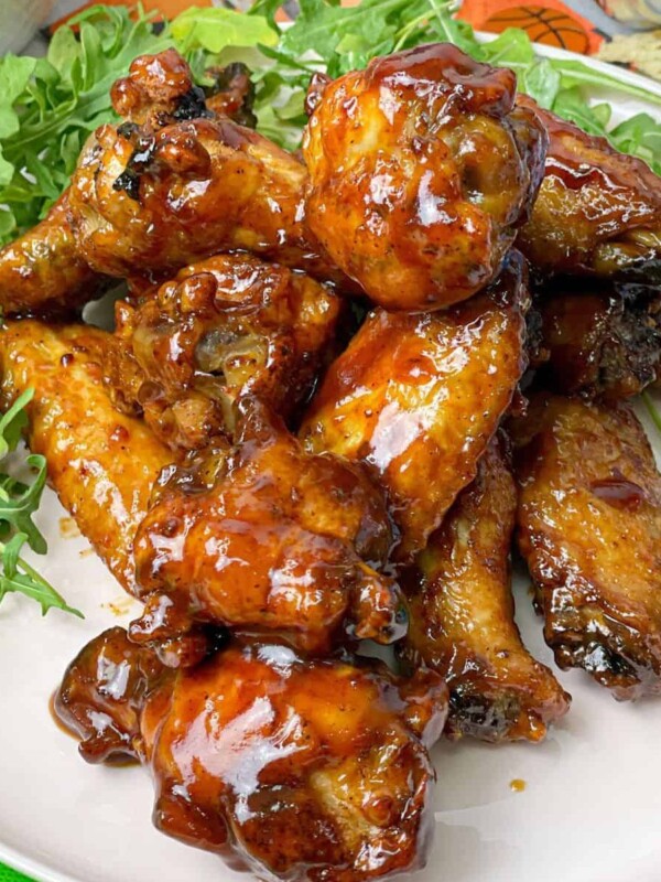 Glossy BBQ chicken wings placed in a white plate with some greens on the side.