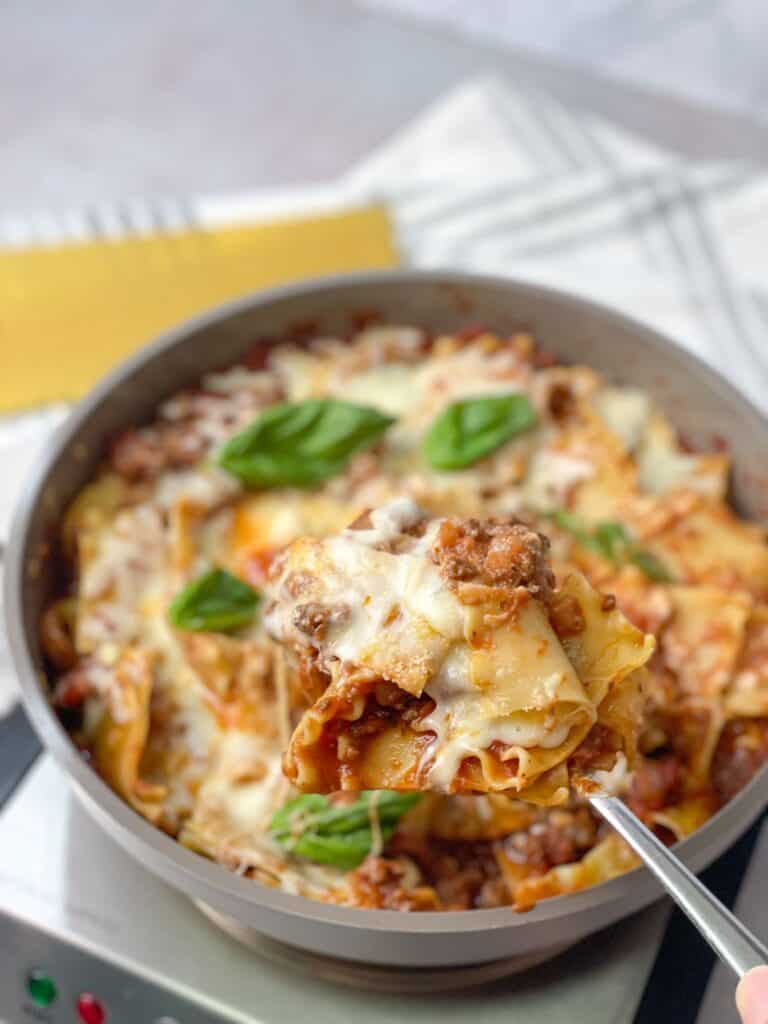 A spoonful of stovetop lasagna taken from a skillet of lasagna topped with mozzarella cheese and basil